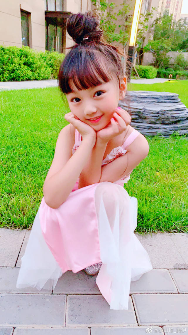 扎起丸子头,换上粉色连衣裙的小山竹,双手托腮对镜