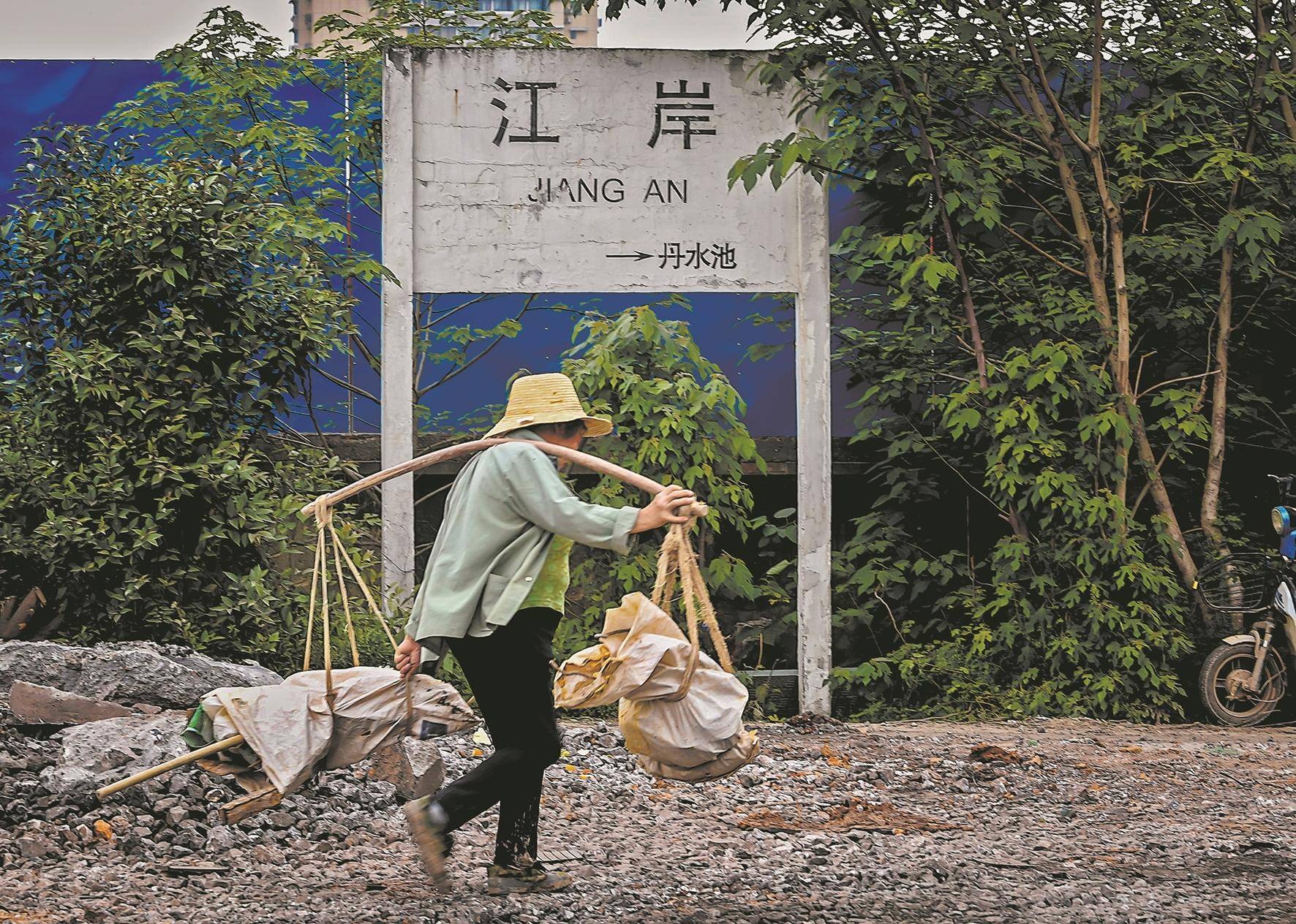 一位挑担老人从老式站牌前走过