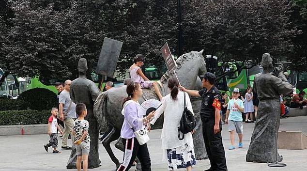 游客攀爬景区的雕塑拍照，保安喊话劝告无效，沉默地递上一牌子