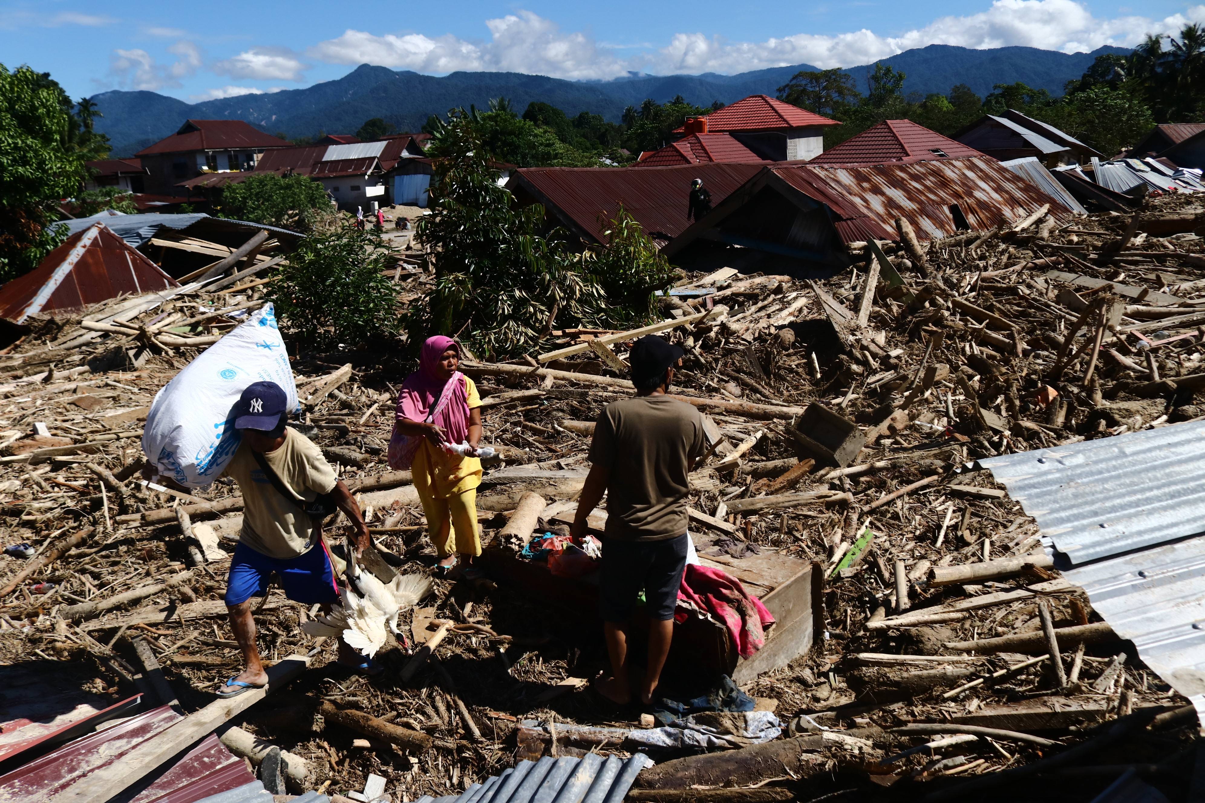 7月17日,人们在印度尼西亚南苏拉威西省北陆屋县被洪水摧毁的房屋残骸