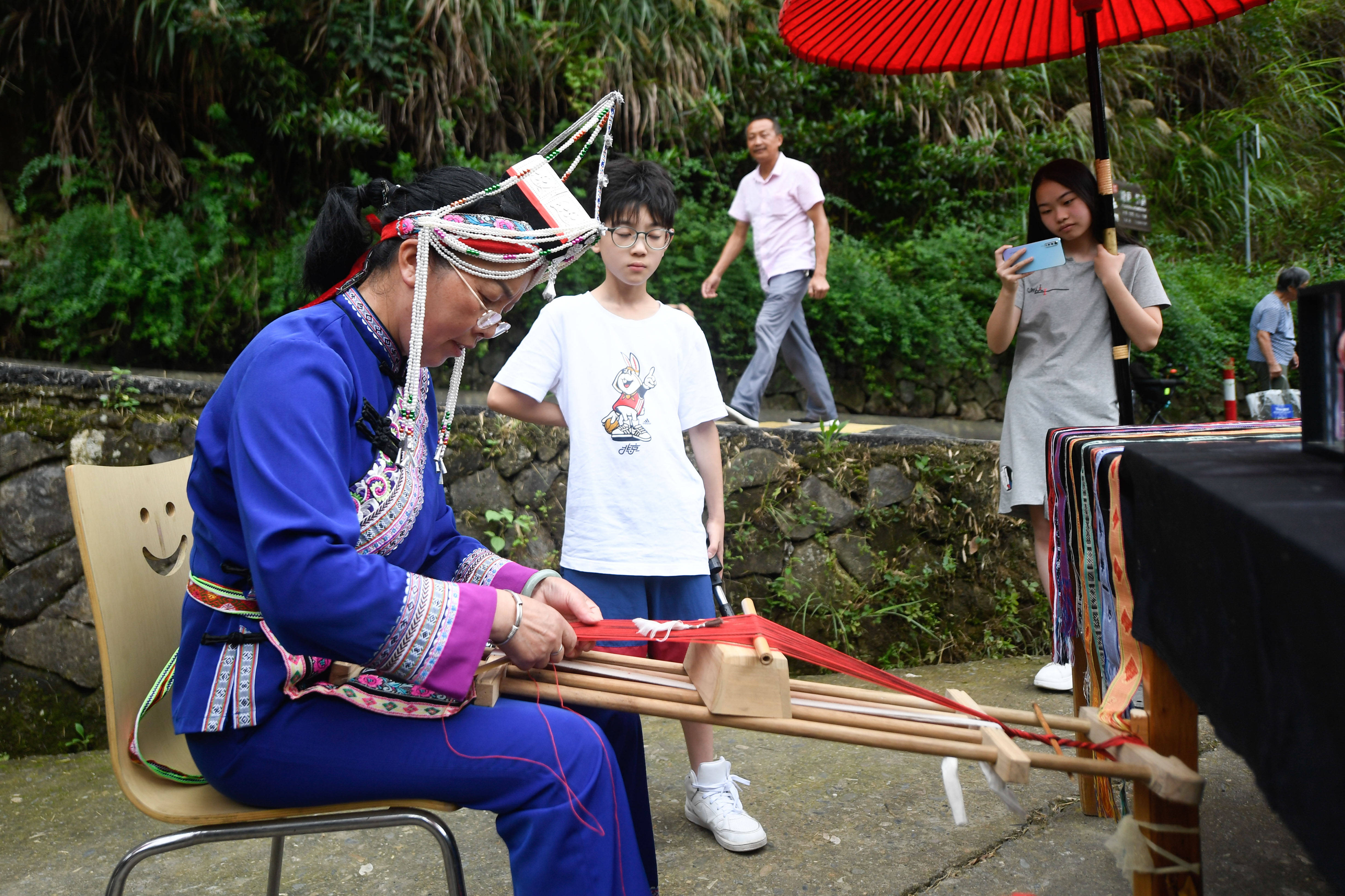 7月18日,遊客在戴家山村觀看畲族綵帶編織技藝.