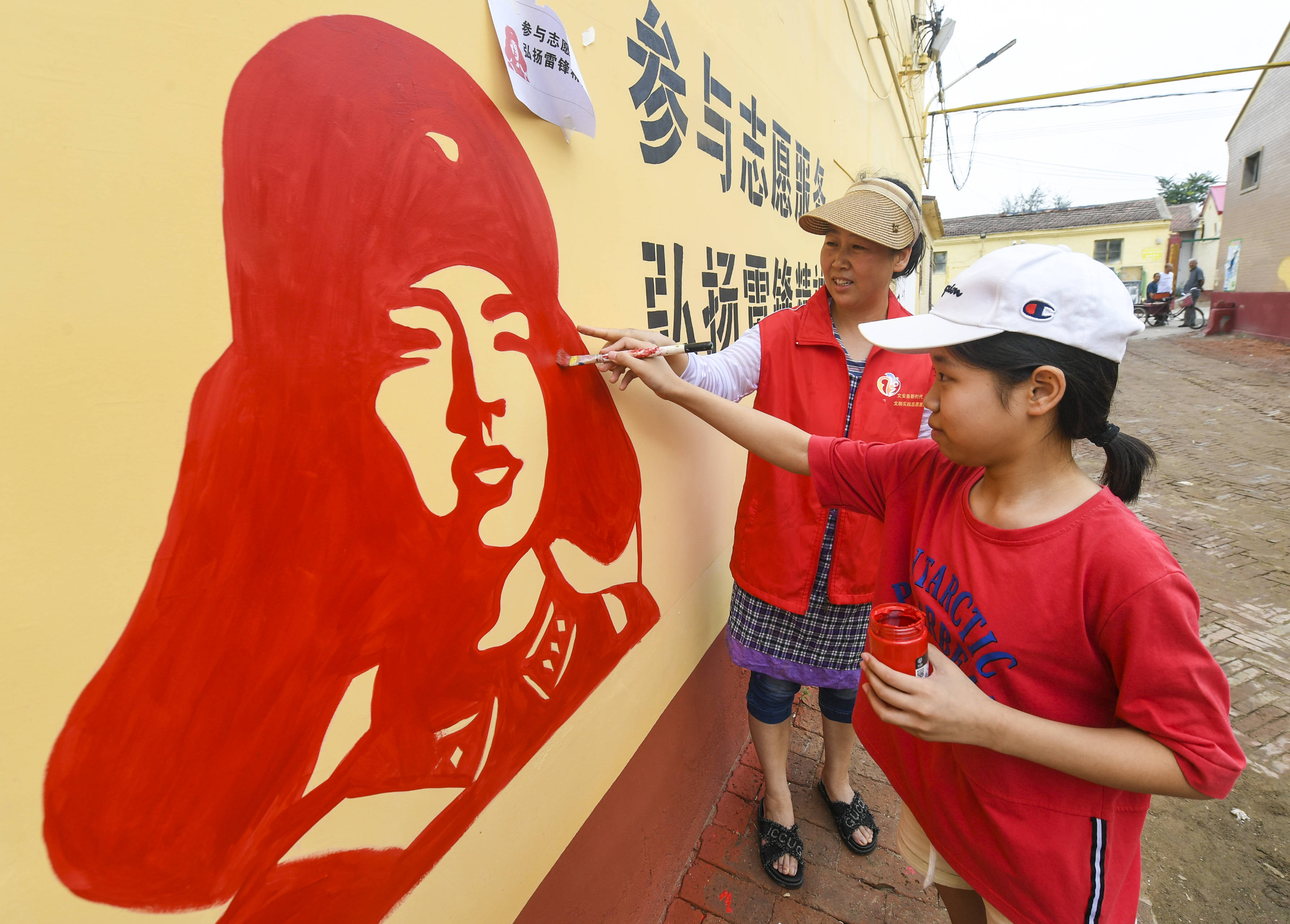 8月8日,在文安縣文安鎮東關村,志願者指導小學生為牆繪作品上色.