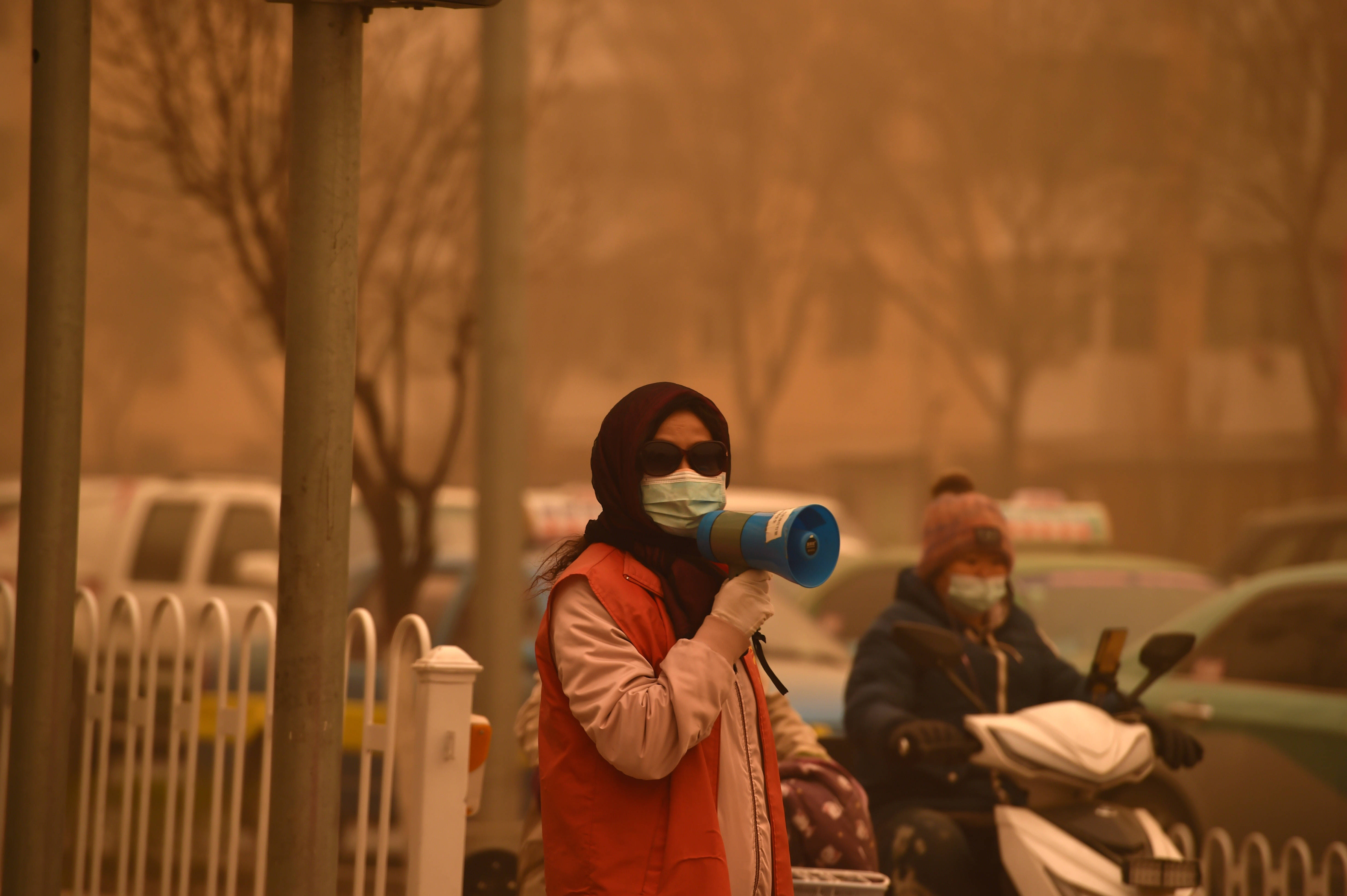 3月15日,在宁夏银川市,志愿者在沙尘中引导市民出行.
