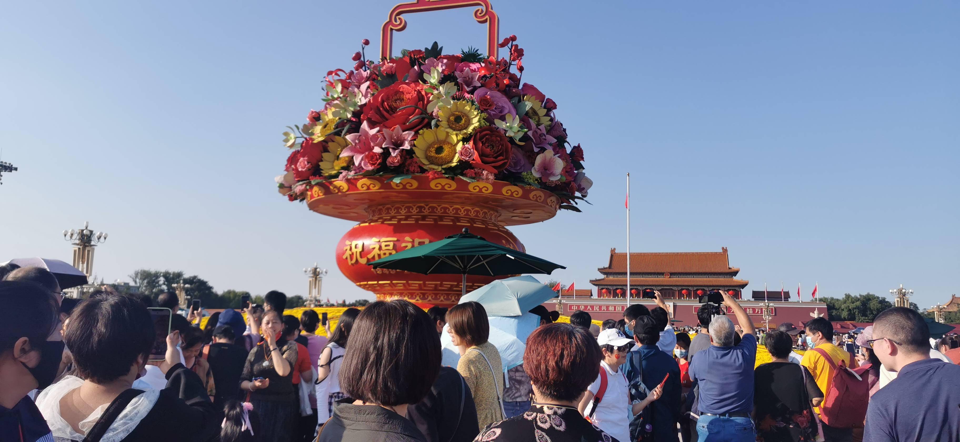 举家出游争相合影,游人在广场大花篮前拍全家福