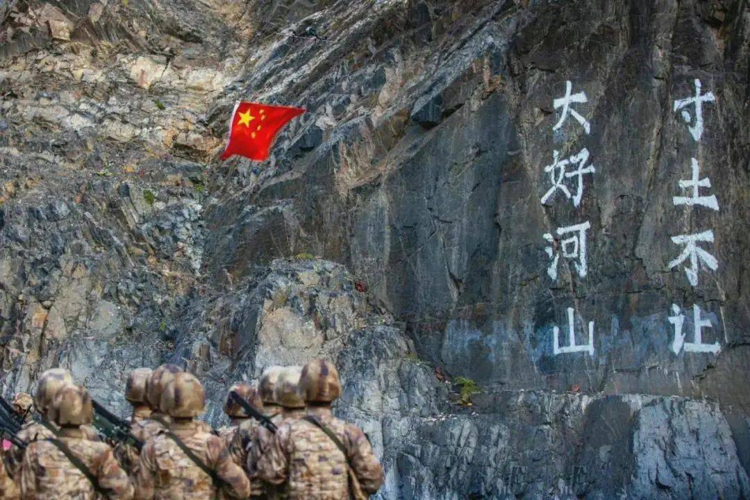 无人机搭载五星红旗缓缓升起,在写着「大好河山寸土不让」的崖壁前