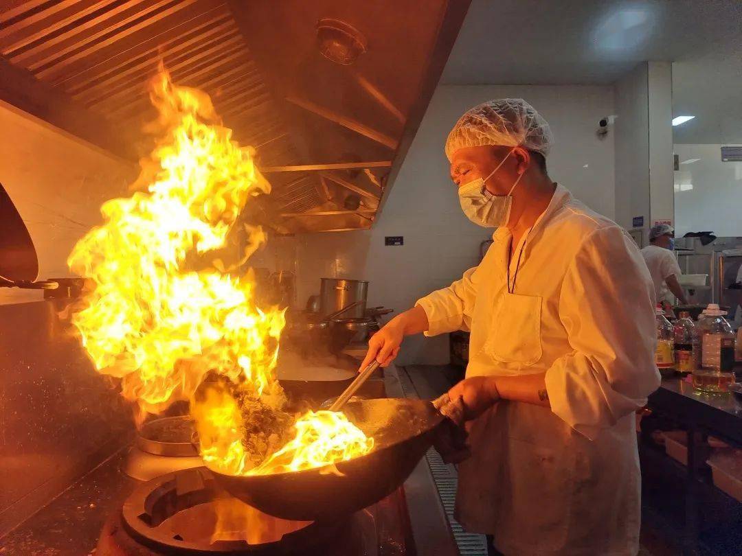 厨师周永健正在炒锅前用铲子翻炒着当天中午的饭菜在炉火旁高达60℃的